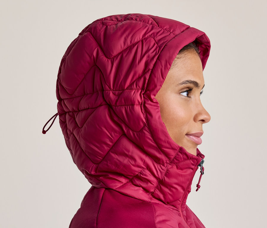 Frau im Profil, die eine pinkfarbene, gesteppte Jacke mit hochgezogener Kapuze trägt und nach rechts blickt.