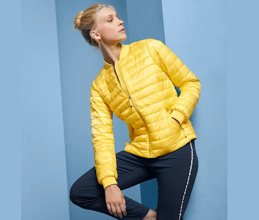 Blonde Frau posiert in gelber Steppjacke.