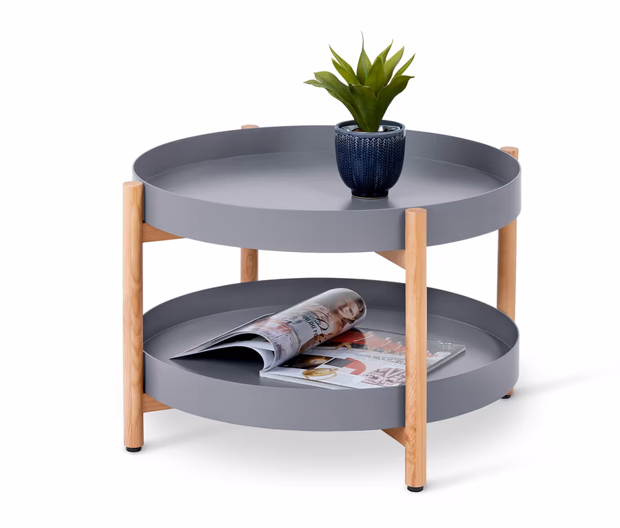 Ein runder Couchtisch mit Extra-Ablage in Grau mit einer Pflanze und einer Zeitschrift darauf.