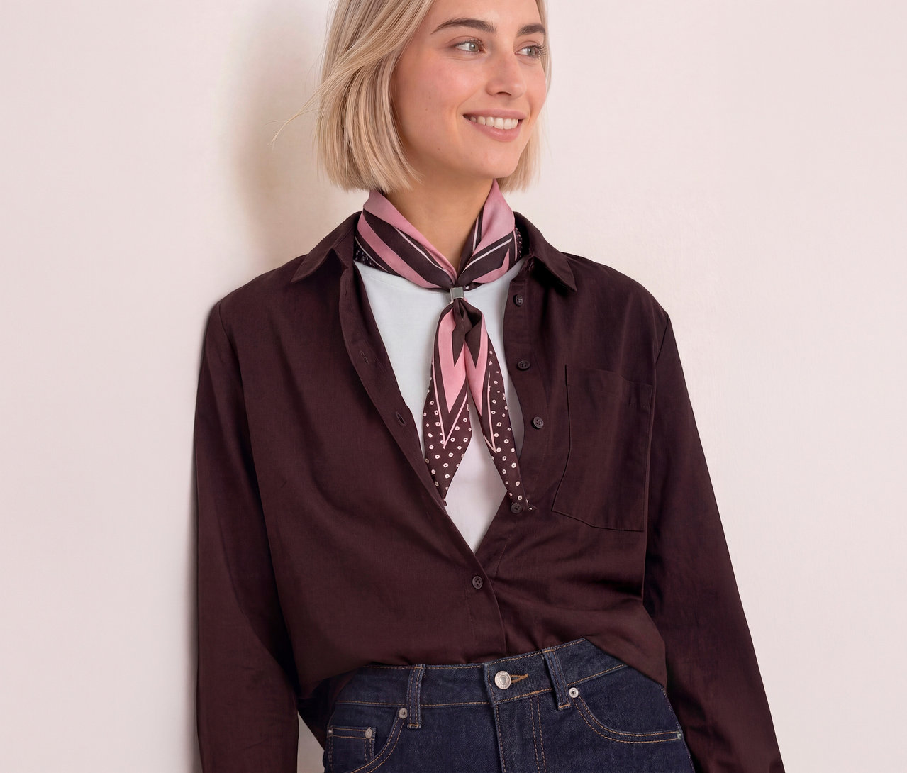 Lächelnde Frau mit kurzem blondem Haar, die ein braunes Hemd, Jeans und ein pink-braunes Street One Bandana trägt.