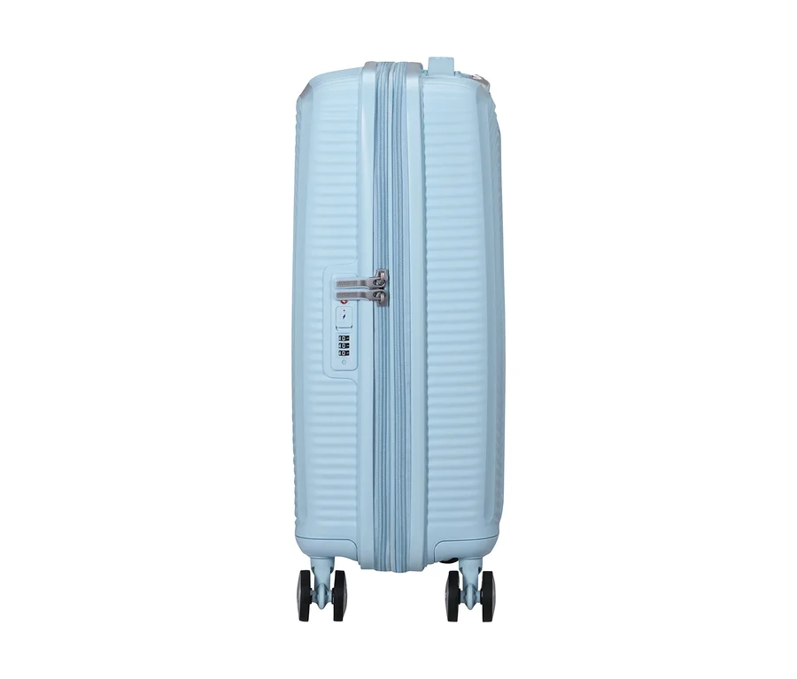 Hellblauer American Tourister Soundbox Hartschalen-Koffer mit Reißverschluss, Zahlenschloss und vier Rollen, von der Seite gezeigt.