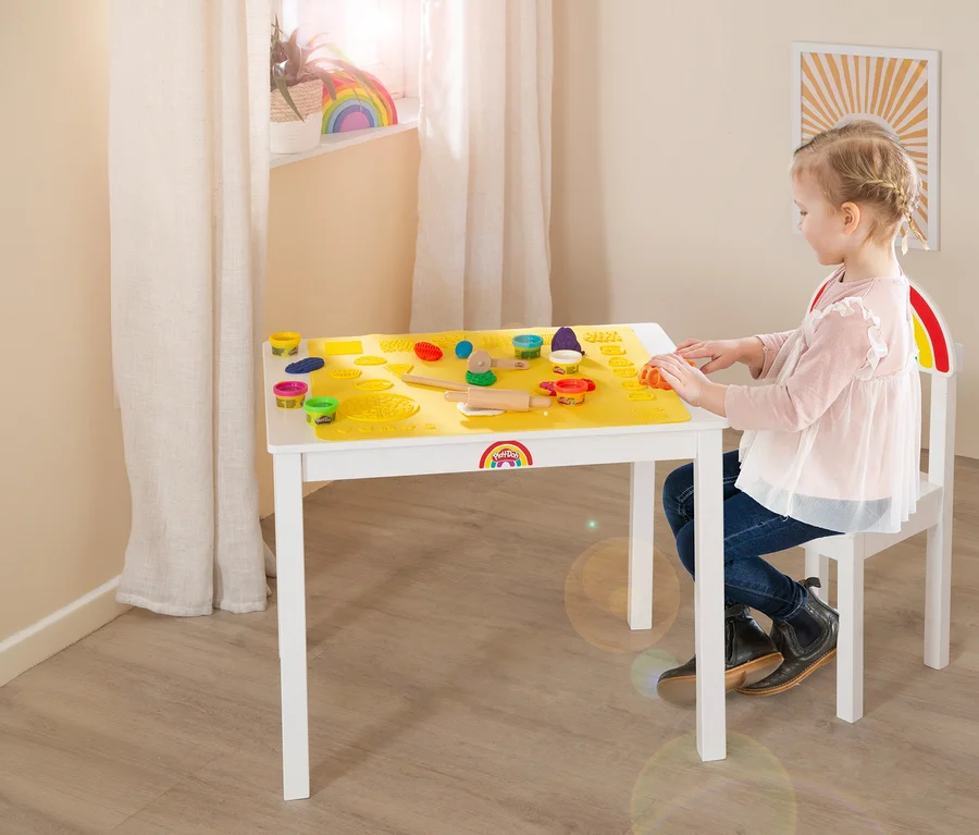 Mädchen spielt am roba x Play-Doh Sitzgruppen-Set mit Knete und Förmchen auf gelber Unterlage.