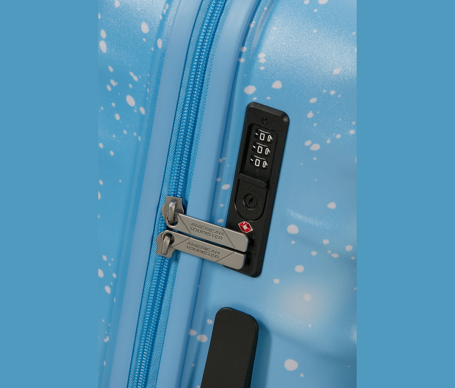 Nahaufnahme eines hellblauen Koffers mit weißen Sprenkeln, der einen blauen Reißverschluss, zwei silberne „AMERICAN TOURISTER“ Zipper und ein integriertes schwarzes Zahlenschloss mit der Einstellung „000“ und einem roten TSA-Logo zeigt.