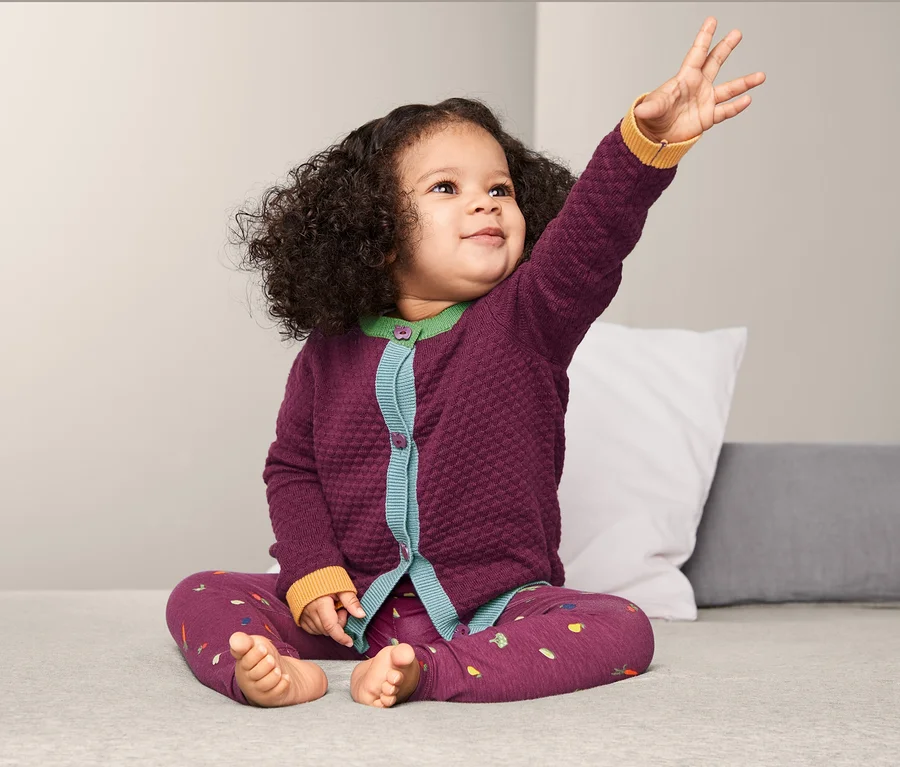 Mädchen sitzt mit erhobenem Arm und trägt eine Strickjacke.