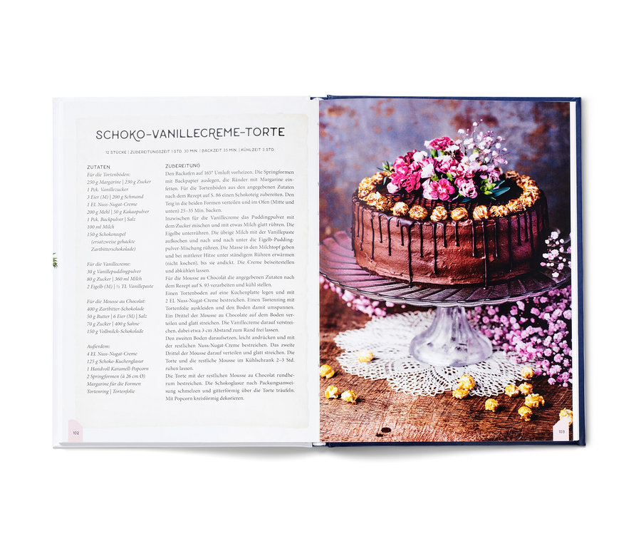 Aufgeschlagenes Kochbuch zeigt Schoko-Vanillecreme-Torte, dekoriert mit Blumen und Popcorn.