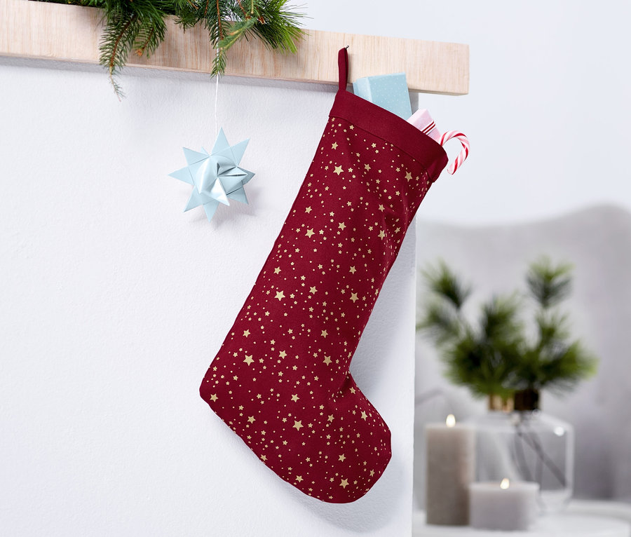 Ein weinroter Weihnachtsstrumpf mit goldenen Sternen hängt an der Wand.