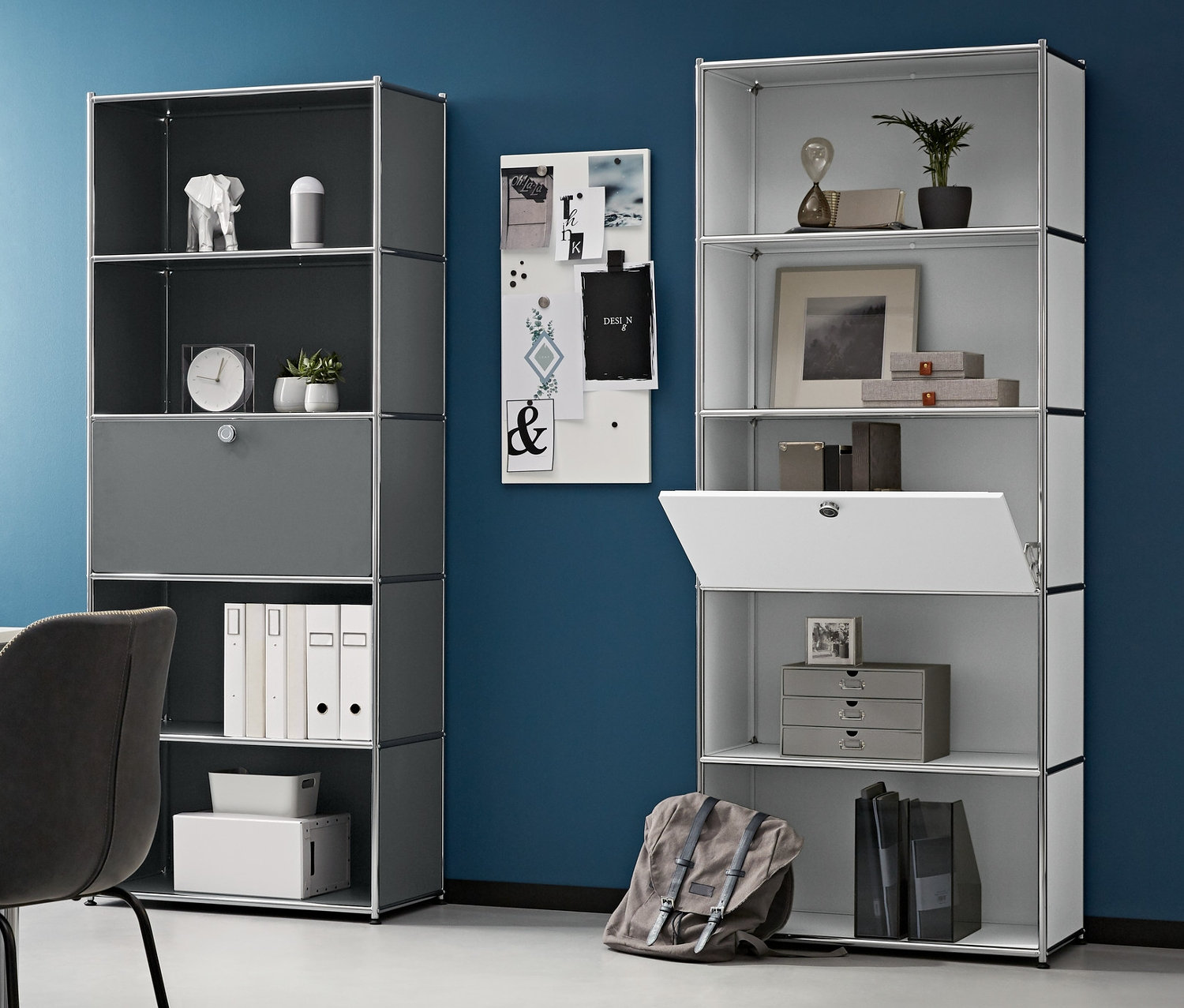 Zimmer mit Schreibtisch, Stuhl und zwei hohen Metallregalen mit einem versetzbaren Klappenfach. Links steht ein Metall-Rollcontainer, auf dem Tisch ein Laptop.