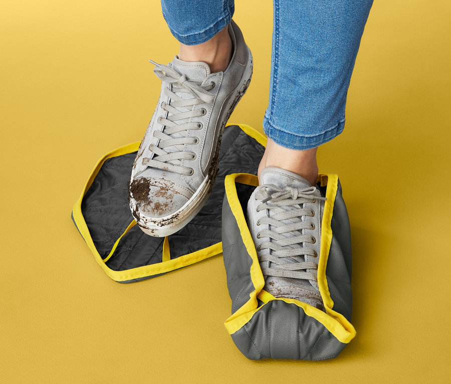 Beine in Jeans. Ein Schuh steht auf einem Schuh-Überzieher, der andere trägt einen Überzieher.