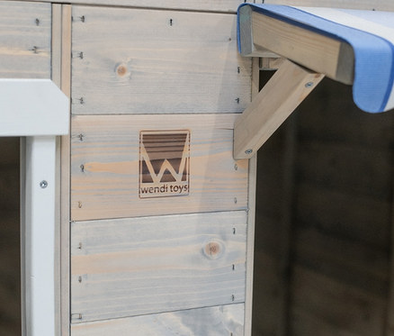 Detailansicht einer Ecke des Wendi-Spielhauses »Maritime House« aus Holzpaneelen mit blau-weiß gestreiftem Vordach.