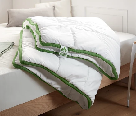 Auf einem Bett liegt ein weißes irisette® greenline Steppbett mit Klimaband.