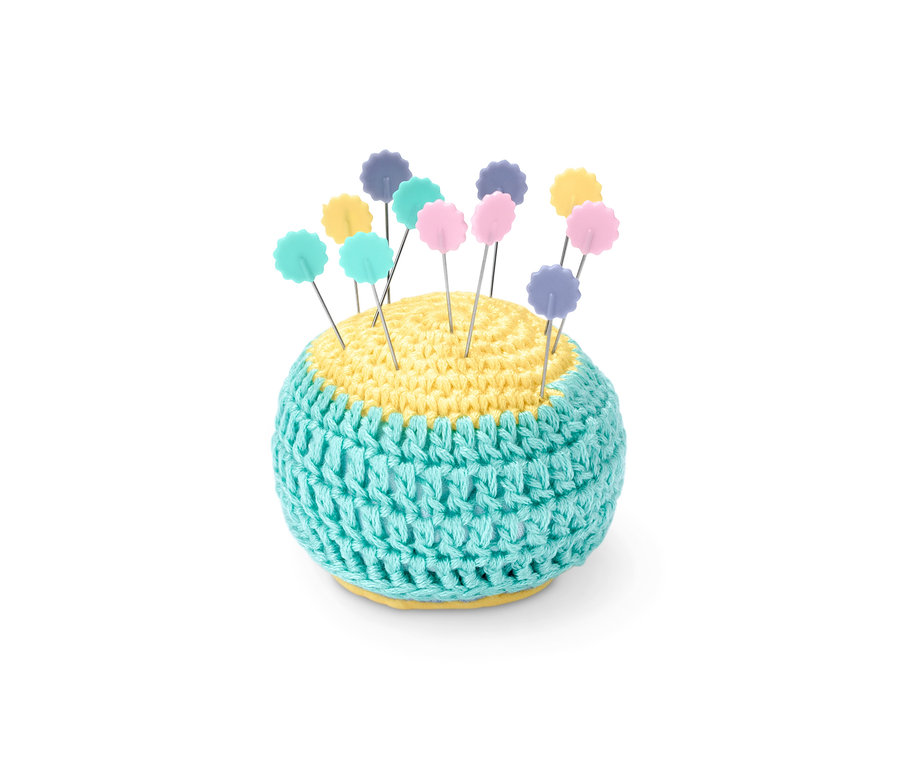Nadeln mit farbigen Köpfen stecken in einem gestrickten Nadelkissen.
