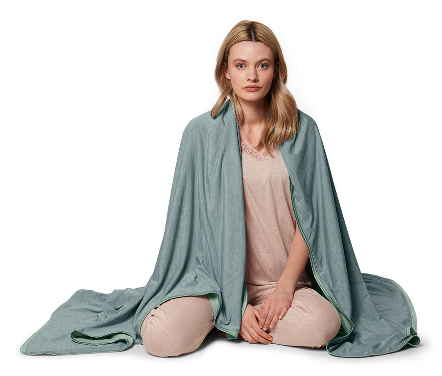 Frau sitzt mit gekreuzten Beinen und ist in eine Kühldecke gehüllt.