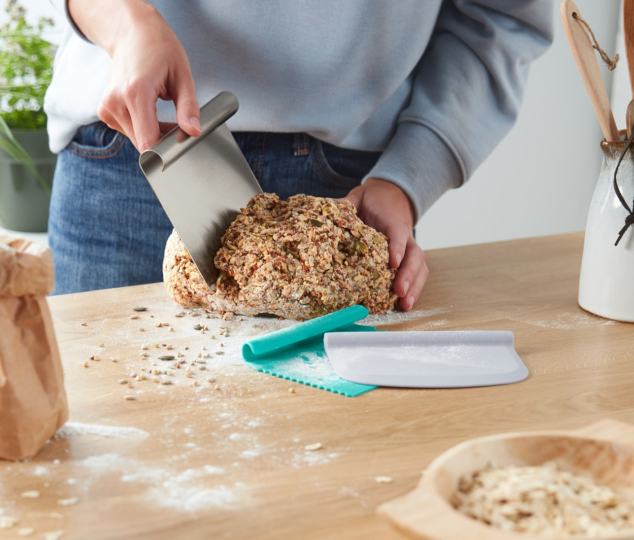 Person schneidet Brot mit dem Profi-Backhelfer-Set auf einem Holztisch.