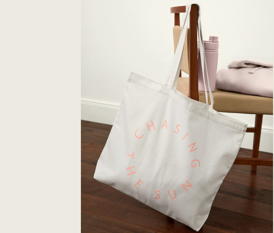 Ein Canvas-Shopper mit der Aufschrift „CHASING THE SUN“ hängt an einem Stuhl. Daneben liegen eine Trinkflasche und ein Sweatshirt.