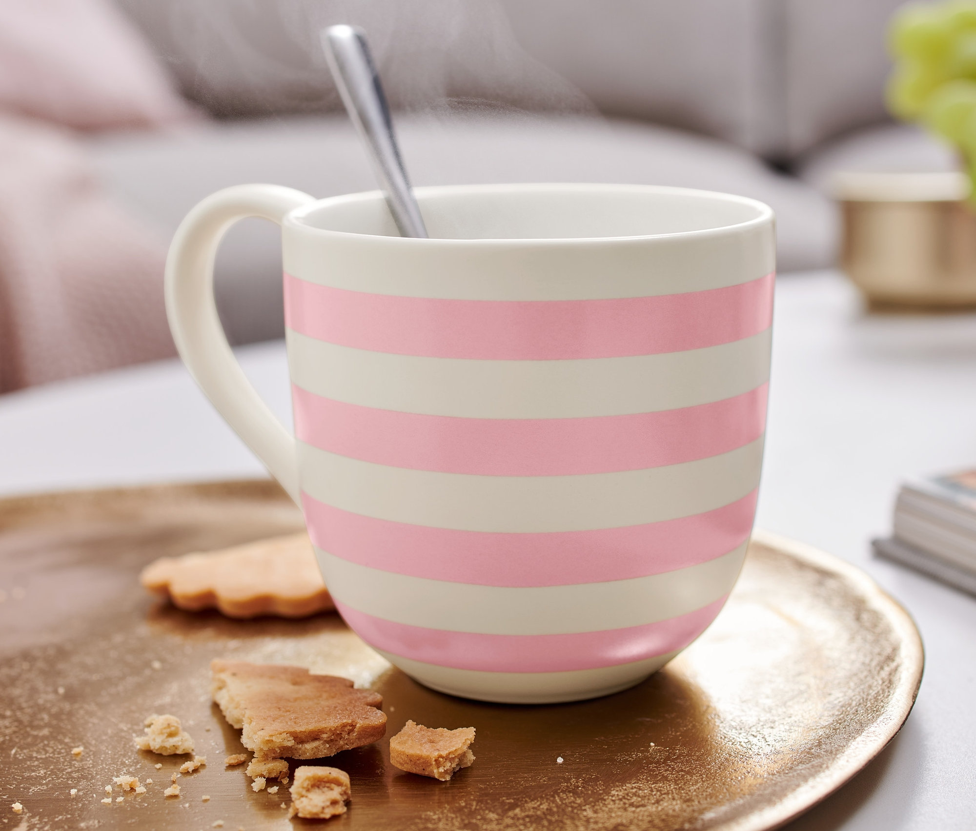 Eine gestreifte Tasse mit einem Löffel auf einem goldenen Tablett mit Keksstücken.