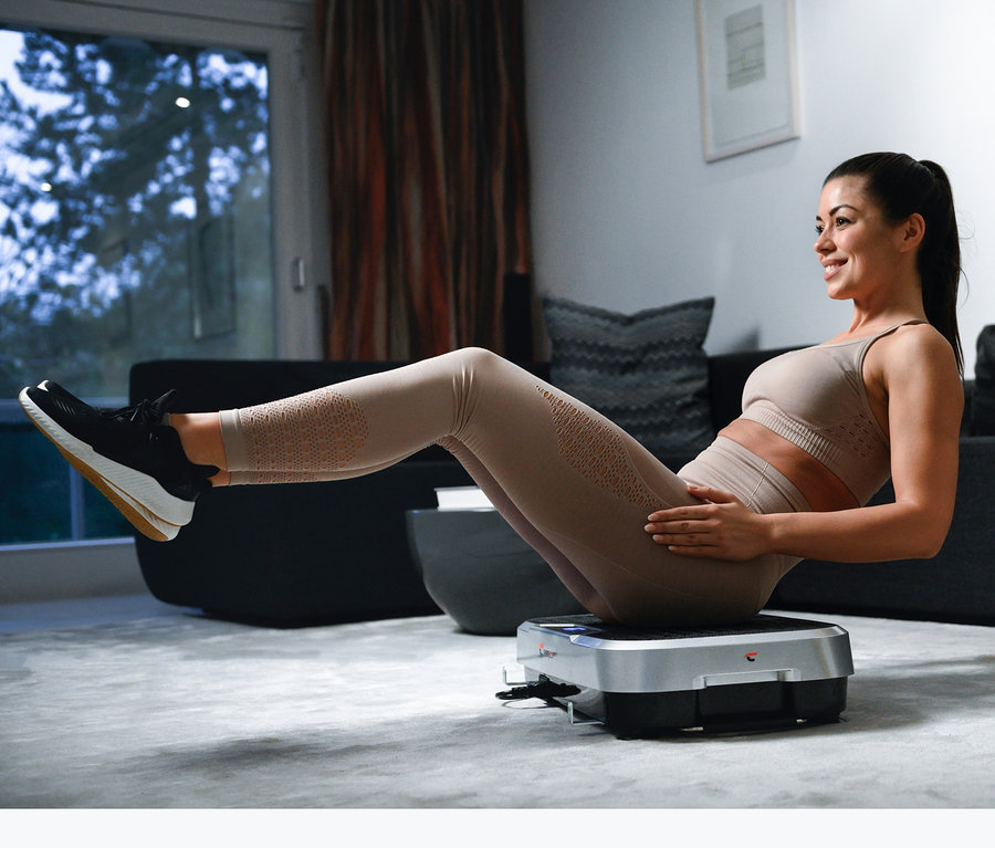 Frau macht Bauchmuskelübungen auf dem Christopeit Vibrationstrainer »Vibro VBT 4200« im Wohnzimmer.