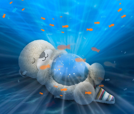 Ein Plüschtier liegt vor blauem Hintergrund mit einer Ozeanprojektion und schwimmenden Fischen. Es handelt sich um den ZAZU-Ozeanprojektor »Otto«.