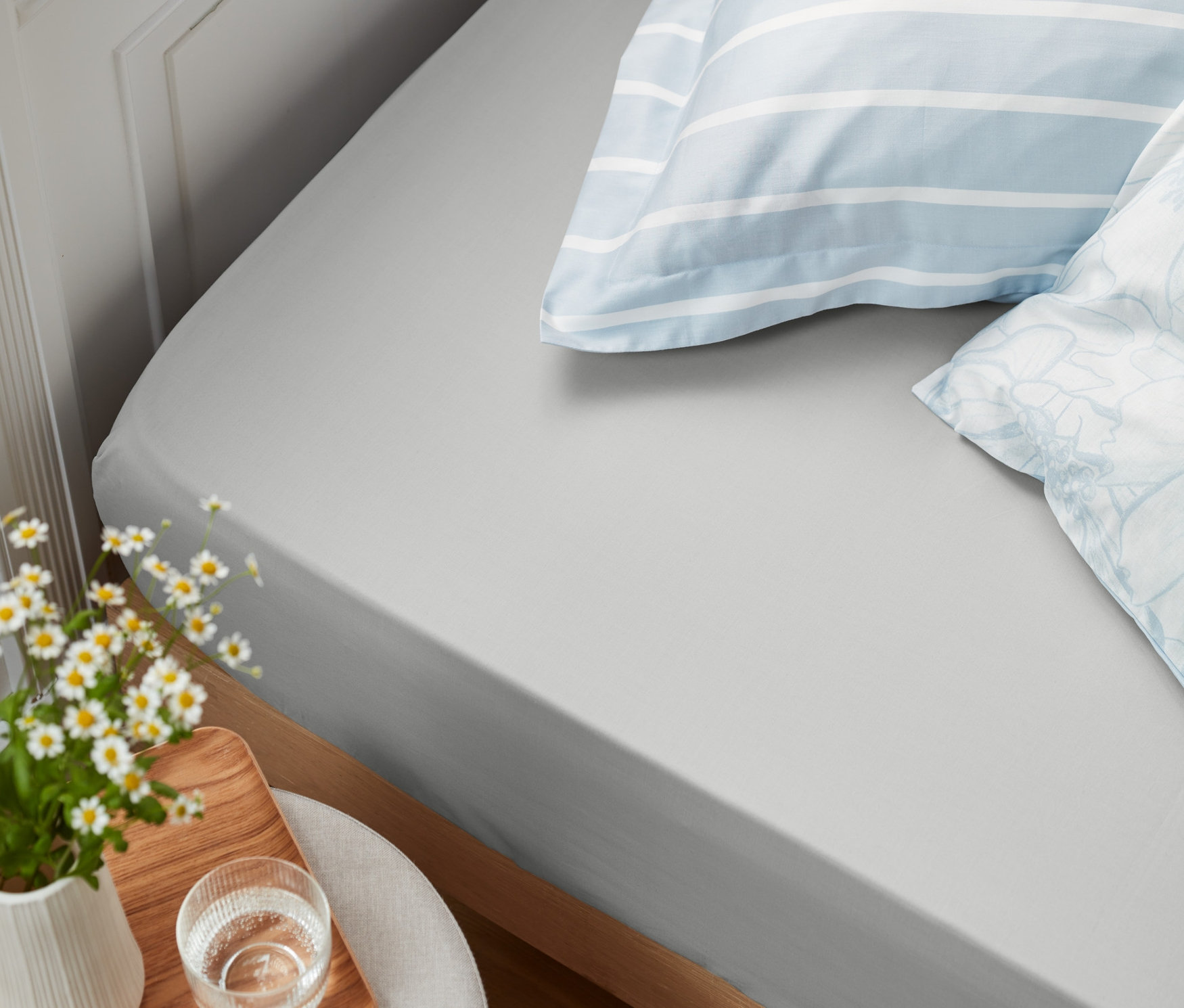 Detailansicht eines Bettes mit grauen Perkal-Spannbettlaken in Normalgröße und Übergröße und zwei Kissen.