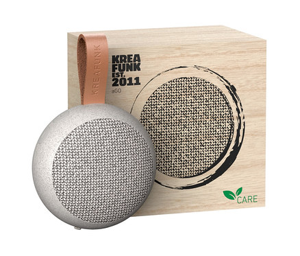 Grauer Kreafunk Care Bluetooth®-Lautsprecher »aGO« neben einer Holzkiste.