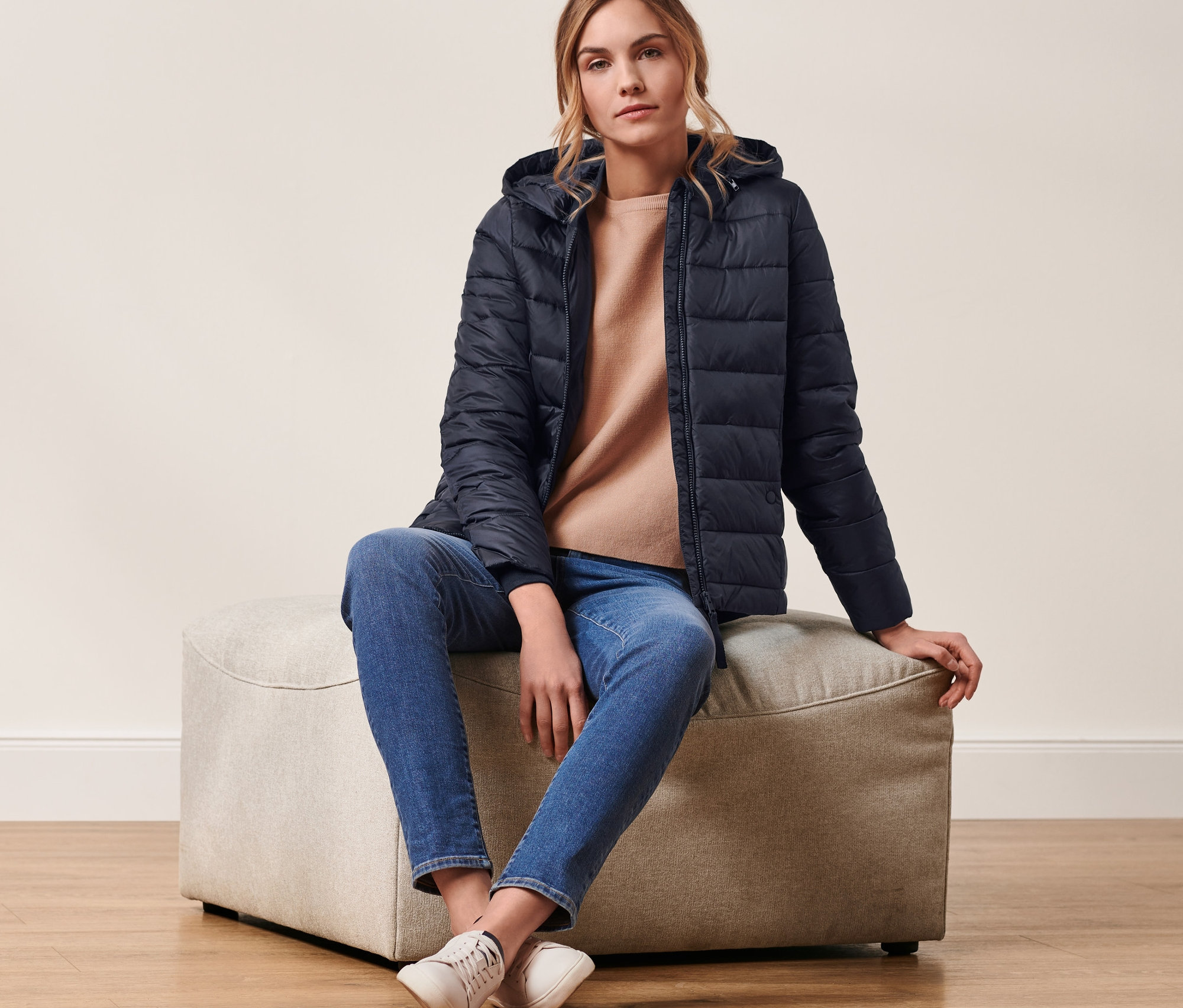 Eine Frau sitzt auf einem Hocker und trägt eine dunkelblaue Steppjacke mit Kapuze.