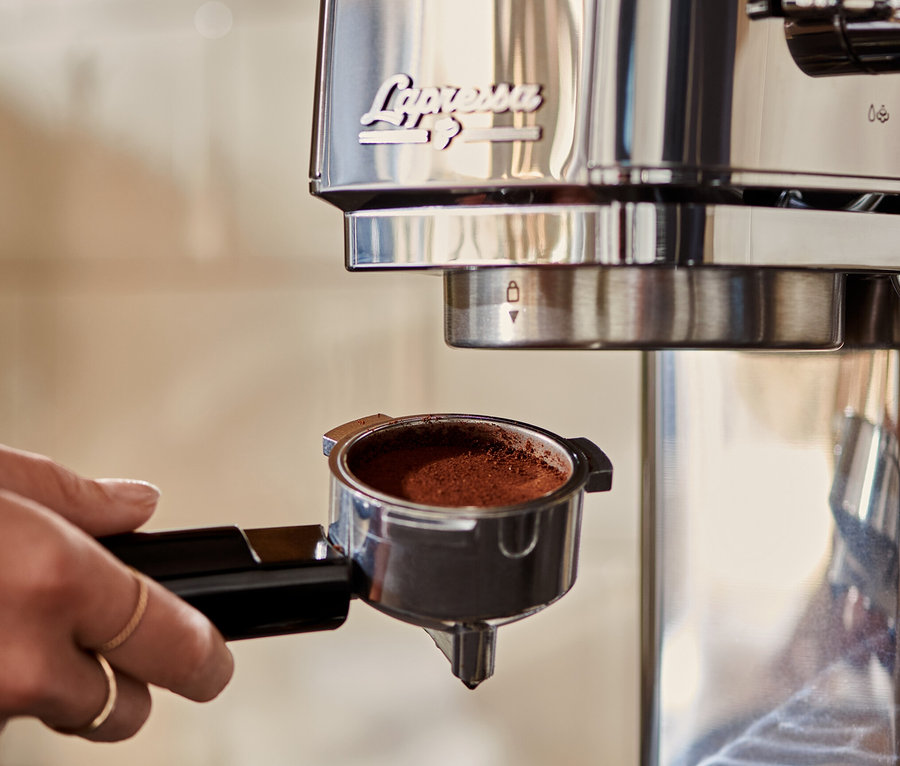 Frau setzt »Lapressa« Siebträgermaschine in Silber mit Kaffee ein.