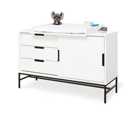 Weiße Pinolino Wickelkommode Steel mit schwarzen Griffen und Beinen. Auf der Kommode liegen ein Elefant, Windeln und ein Schuh.