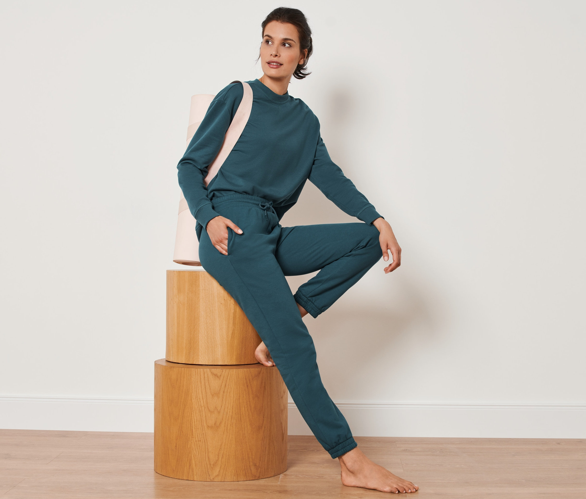 Frau sitzt auf Holzhockern und trägt eine dunkelsmaragdgrüne Sweathose.