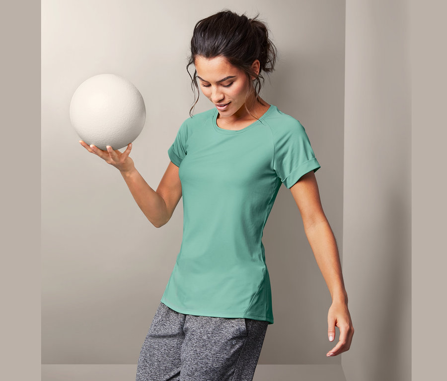 Frau hält einen weißen Ball und trägt ein Sportshirt.