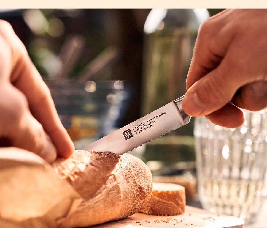 Detail einer Person, die Brot mit einem ZWILLING Messer-Traveller-Set Brotmesser schneidet.