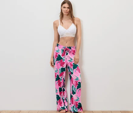 Frau steht und trägt einen weißen Spitzen-BH und eine Relaxhose mit Blumenmuster.