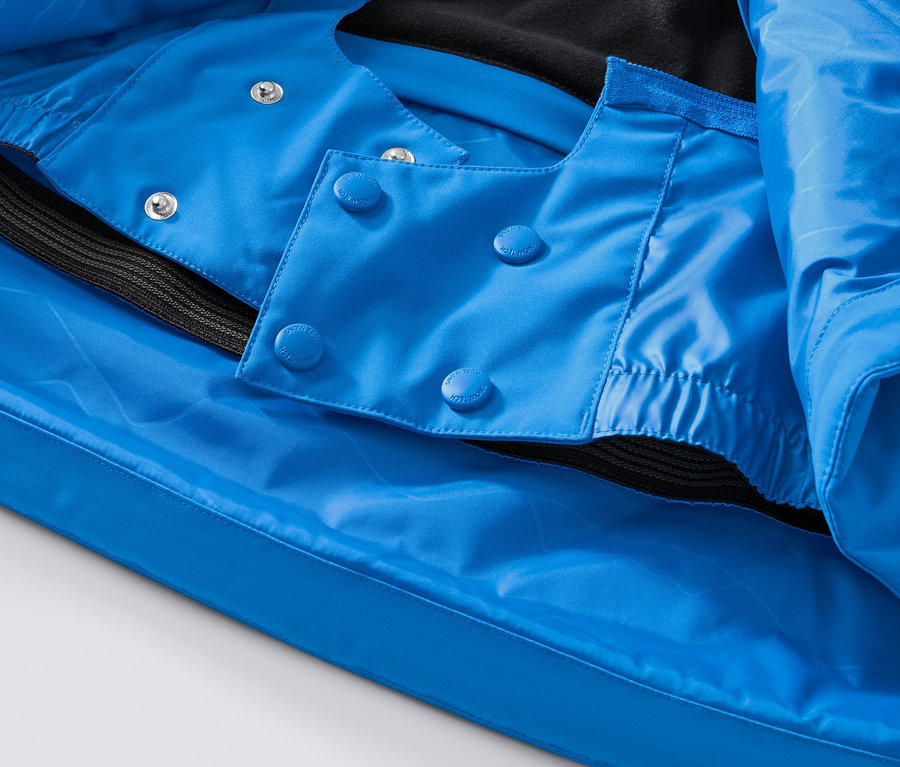 Detailansicht einer blauen High-Tech-Skijacke mit Knöpfen und schwarzem Saum.