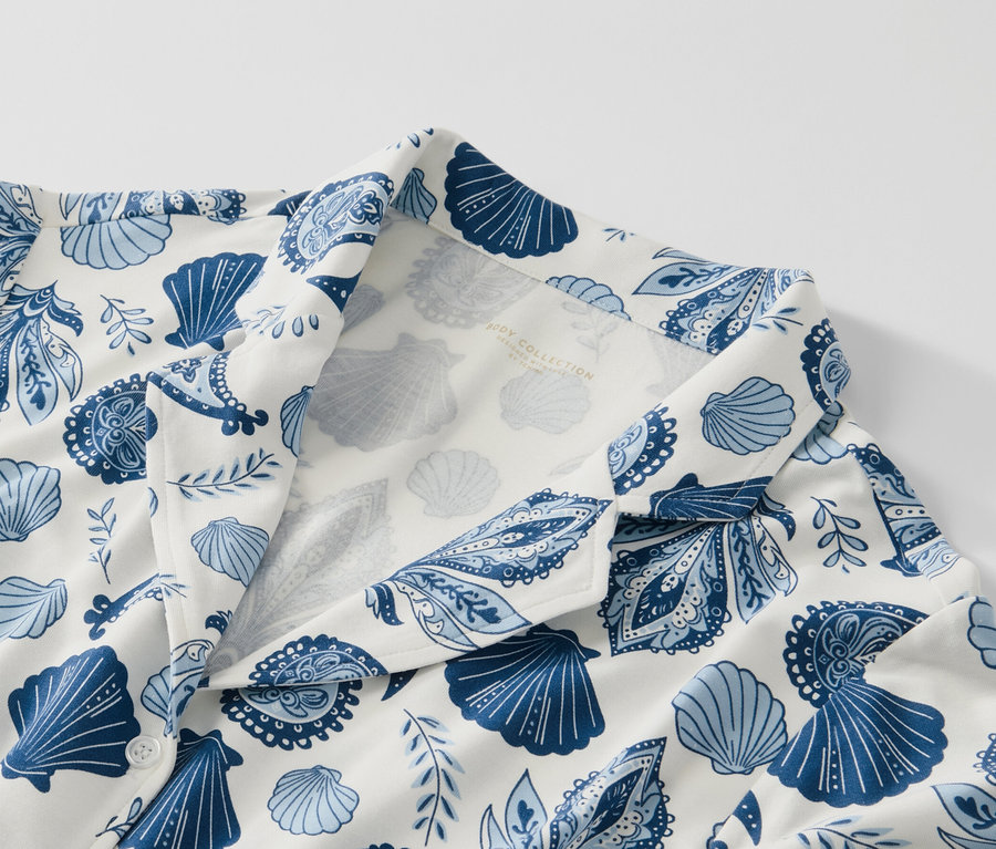 Detailansicht eines Pyjamas mit blauem Muschel- und Paisley-Muster auf weißem Grund.