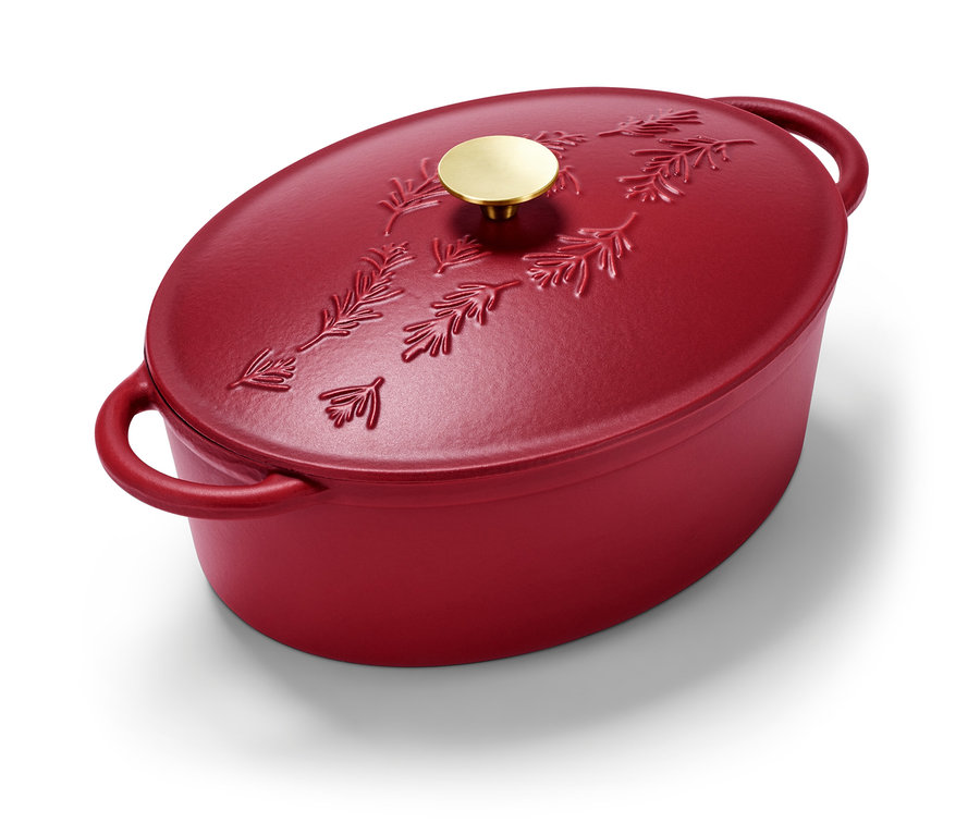 Ein roter, ovaler Gusseisen-Bräter mit Tannenzweigmuster und goldenem Griff.