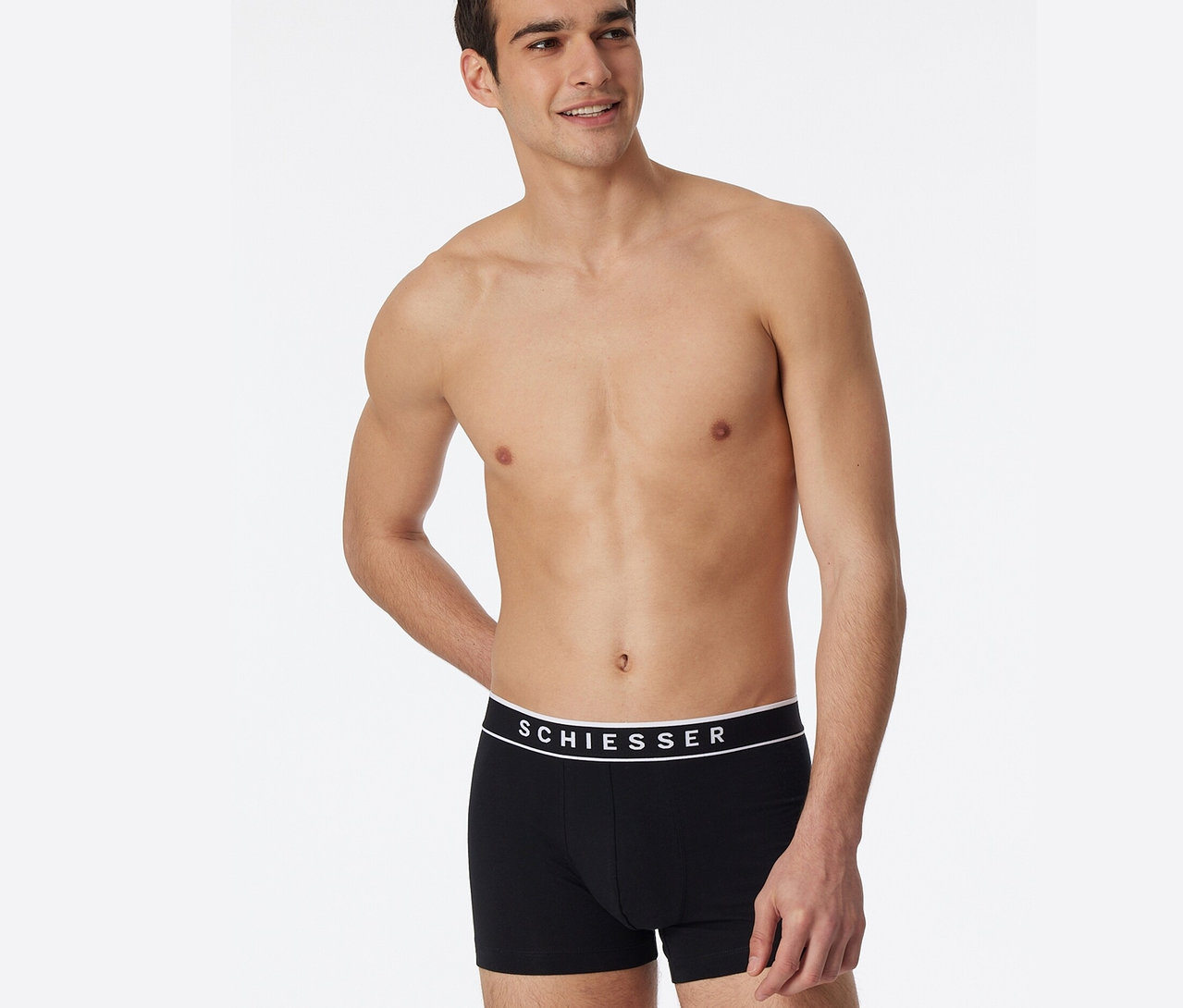 Mann posiert mit freiem Oberkörper in schwarzen 3 SCHIESSER Shorts mit Bio-Baumwolle.
