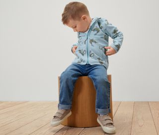 Junge sitzt auf einem Hocker und trägt eine Kinder-Fleecejacke mit Drache.