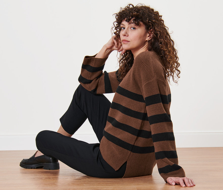 Frau sitzt auf dem Boden und trägt einen gestreiften Strickpullover.