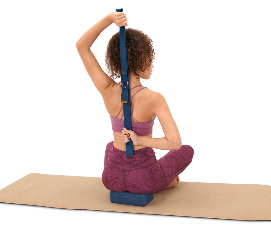 Frau sitzt auf Yogamatte und benutzt Yoga-Set: Block und Gurt.