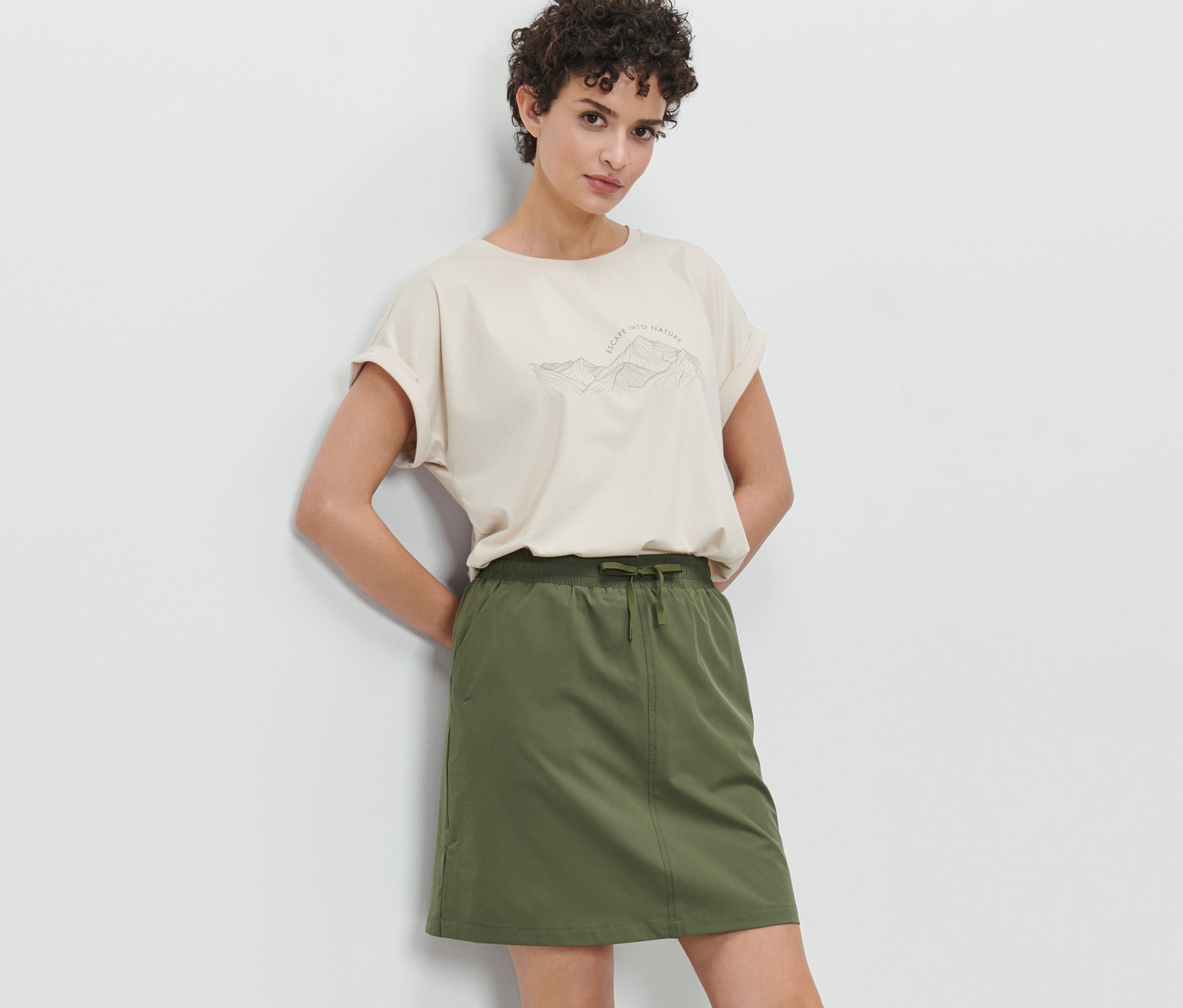 Frau posiert in olivgrünem Funktionsrock mit Shorts und beigem T-Shirt.