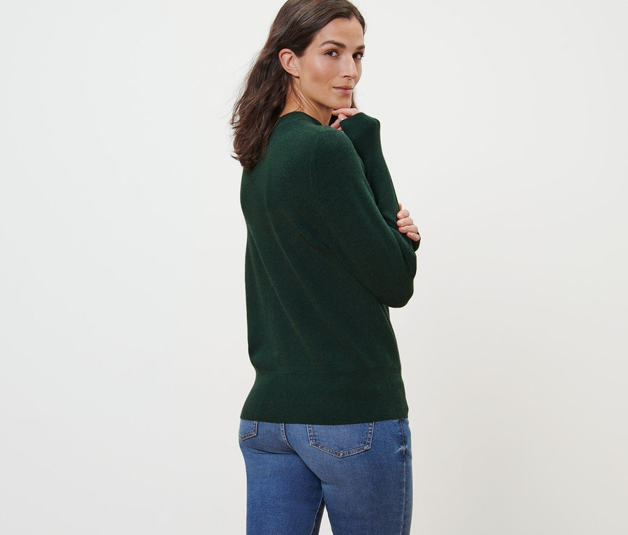 Frau posiert in Feinstrickpullover in Grün und Jeans.