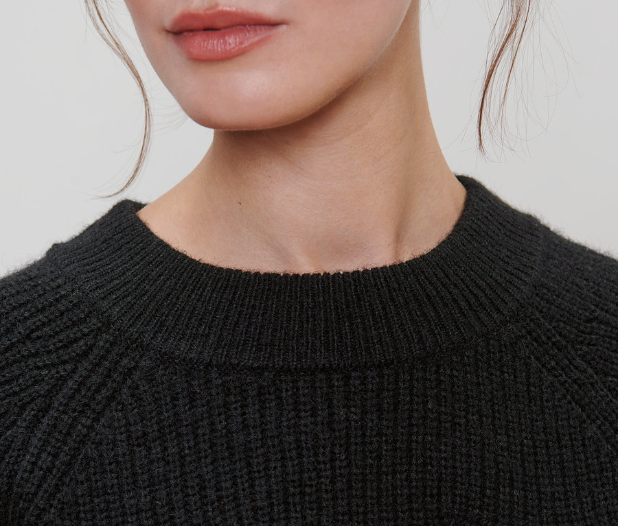 Detailaufnahme einer Dame, die einen schwarzen Strickpullover trägt.