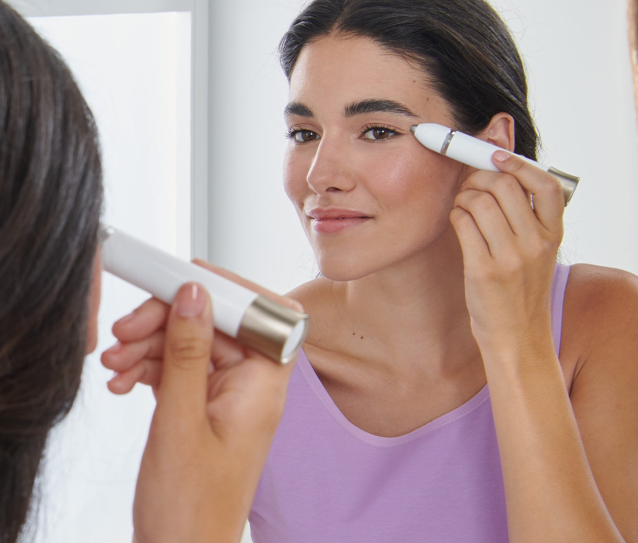 Frau stylt ihre Augenbrauen mit einem elektrischen Augenbrauenstyler vor einem Spiegel.