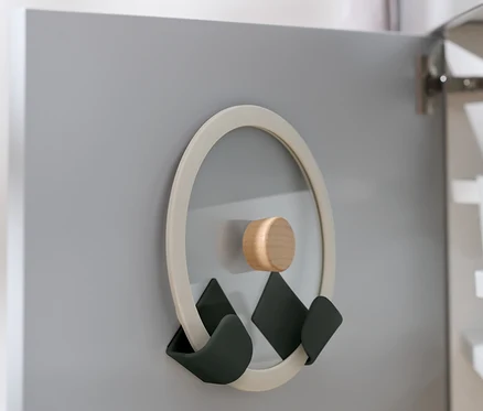 Ein Deckelhalter, 4 Wandhalterungen für Deckel, ist an der Innenseite einer grauen Schranktür befestigt.