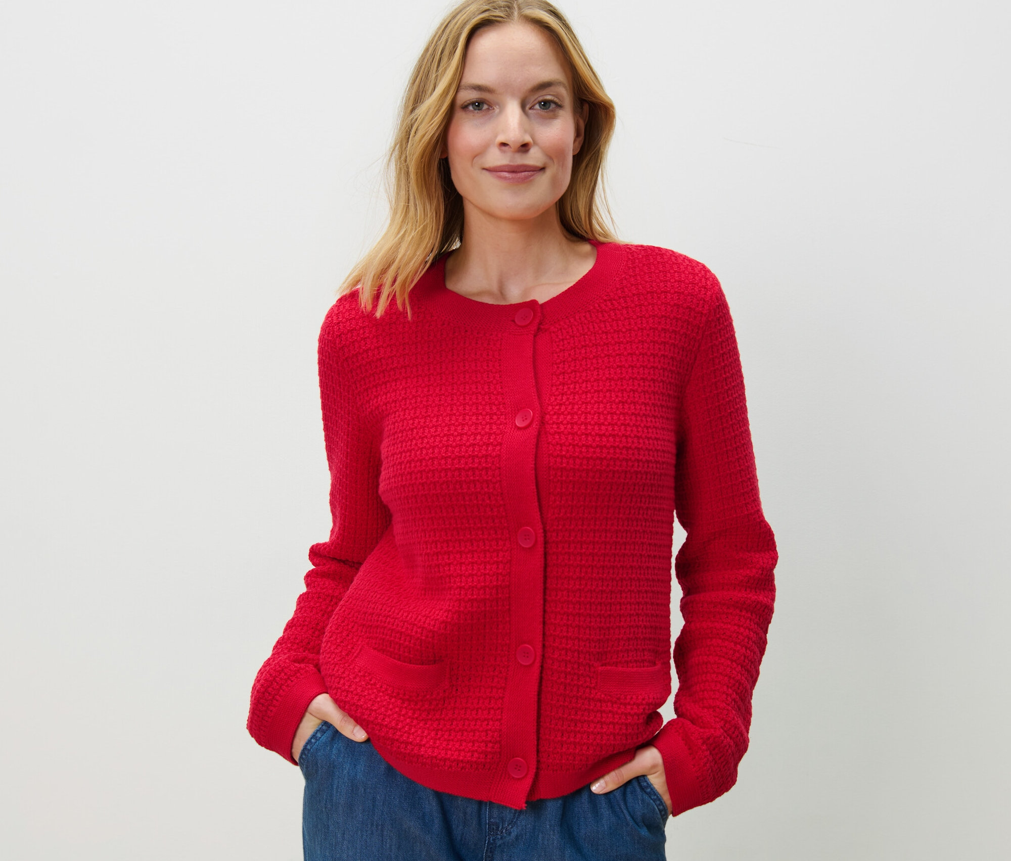 Frau posiert in rotem Cardigan aus Strukturstrick und blauen Jeans.