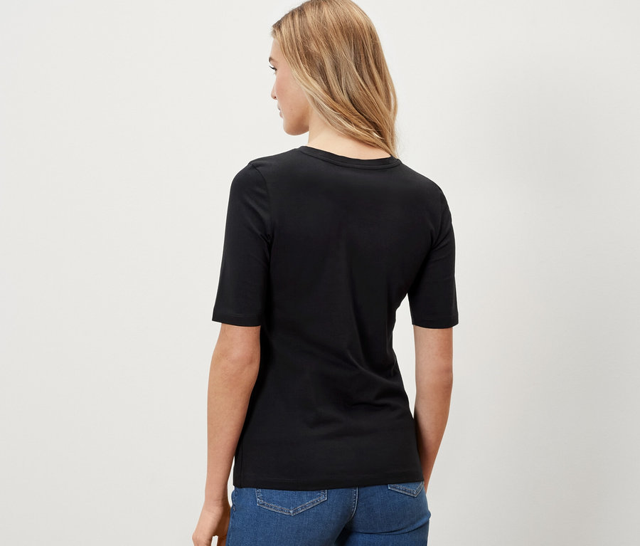 Frau trägt ein schwarzes Halbarmshirt und Jeans.