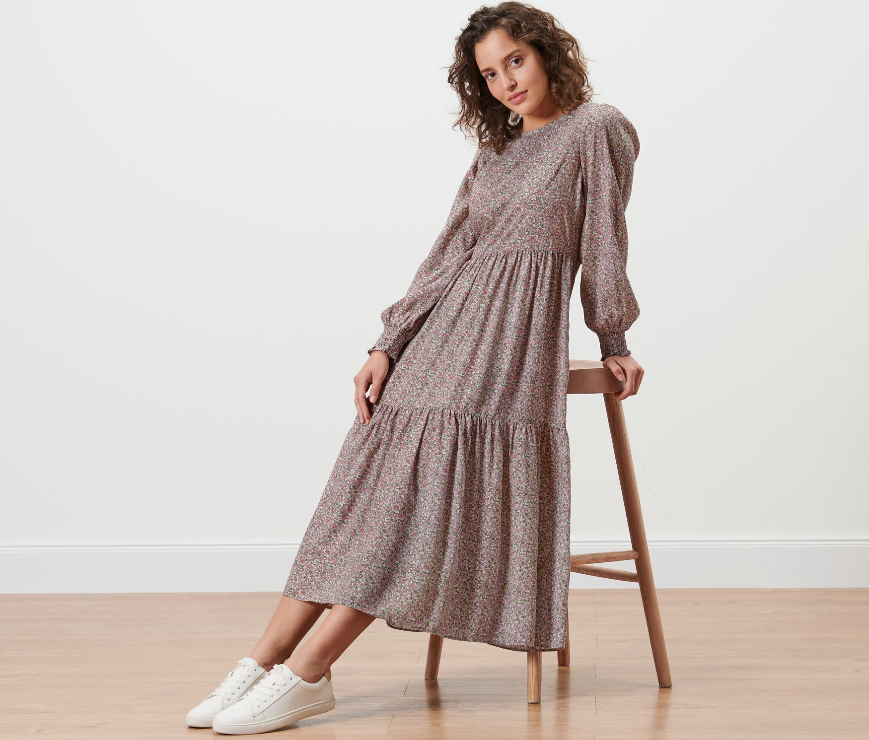 Frau sitzt auf einem Holzhocker und trägt ein florales Midikleid.