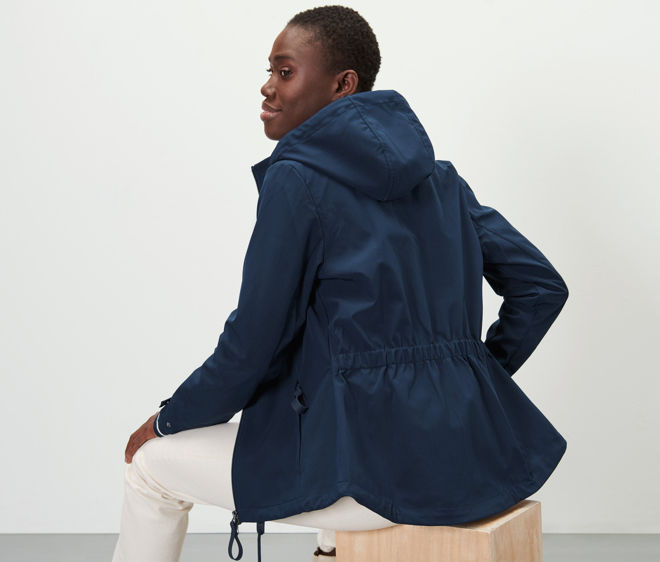 Frau sitzt und trägt eine Softshell-Jacke.