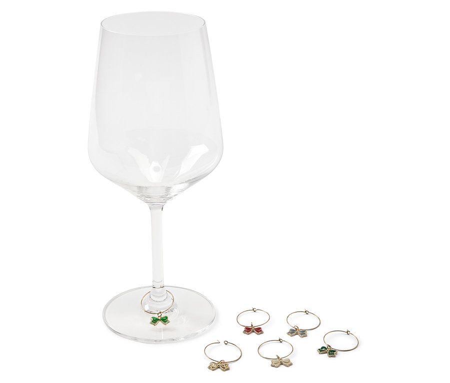 Ein leeres Weinglas mit einem grünen Schmetterling am Stiel und fünf weiteren Schmetterlingen in den Farben Rot, Gold, Blau und Grün daneben.