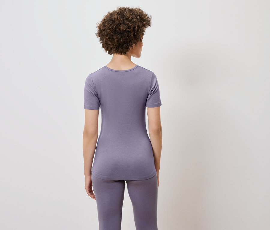 Von hinten ist eine Frau mit lockigem Haar zu sehen, die ein lila T-Shirt und Leggings trägt.