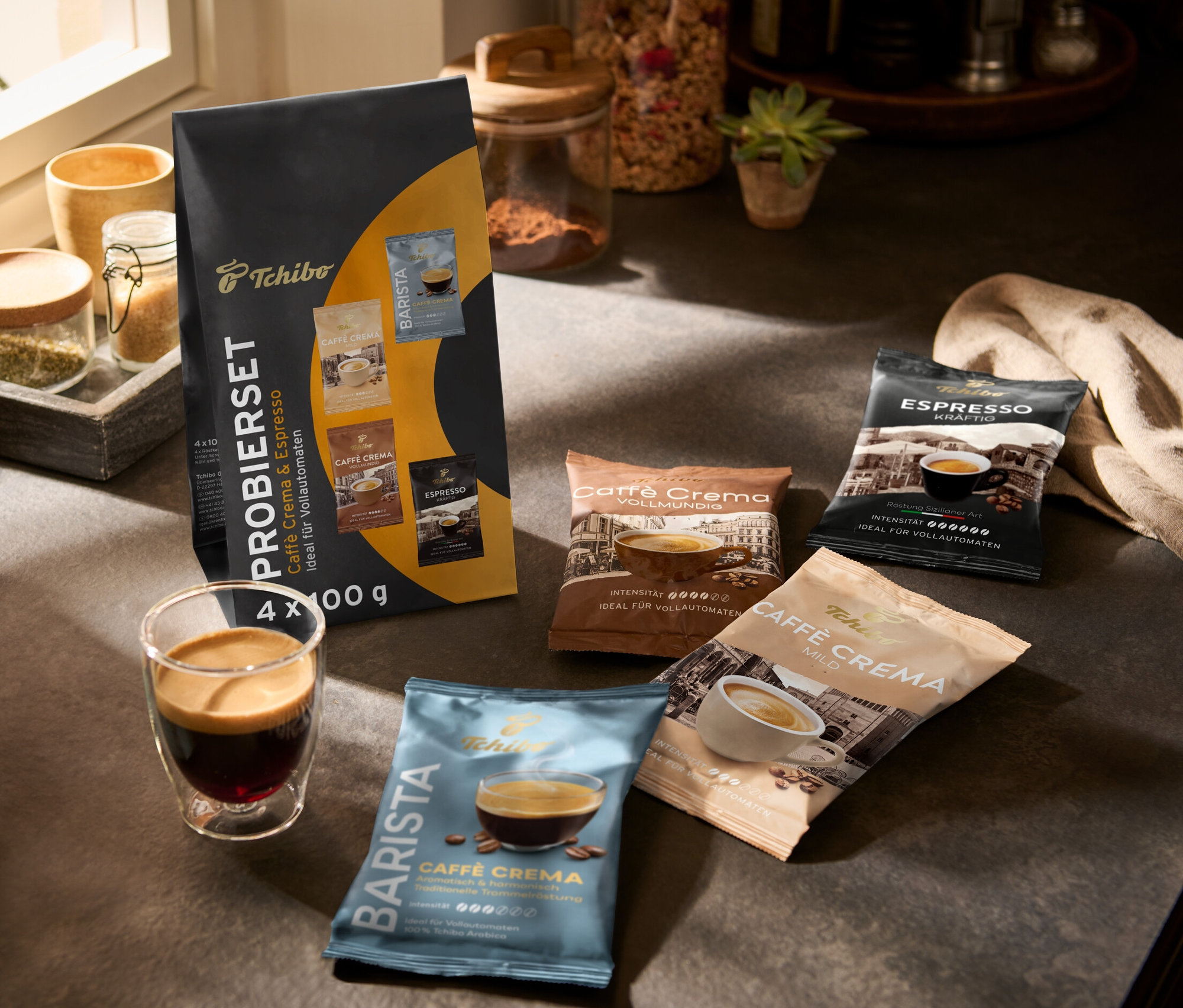 Auf einer Küchentheke stehen eine Tasse Kaffee und eine Packung Caffè Crema & Espresso Probierset - 4x 100 g Ganze Bohne.