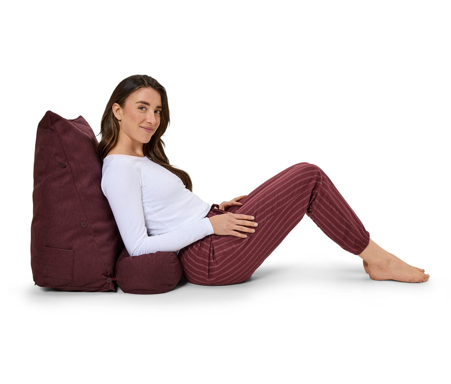 Frau lehnt an einem purpurroten Kissen mit abgestütztem Kopf, gekleidet in gestreiften Hosen und einem weißen Oberteil.